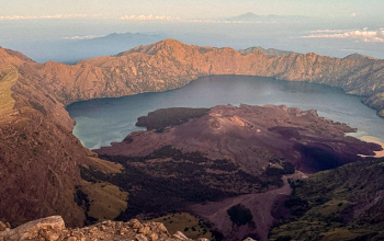 Panoramic view of Mount Rinjani crater lake and volcanic peaks under golden morning light in Lombok, Indonesia