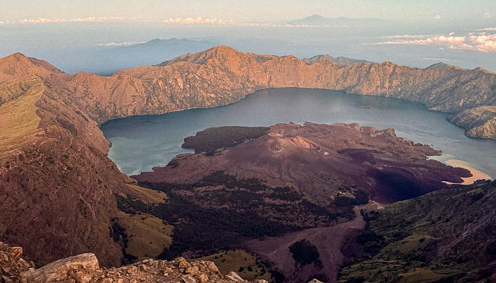 Panoramic view of Mount Rinjani crater lake and volcanic peaks under golden morning light in Lombok, Indonesia